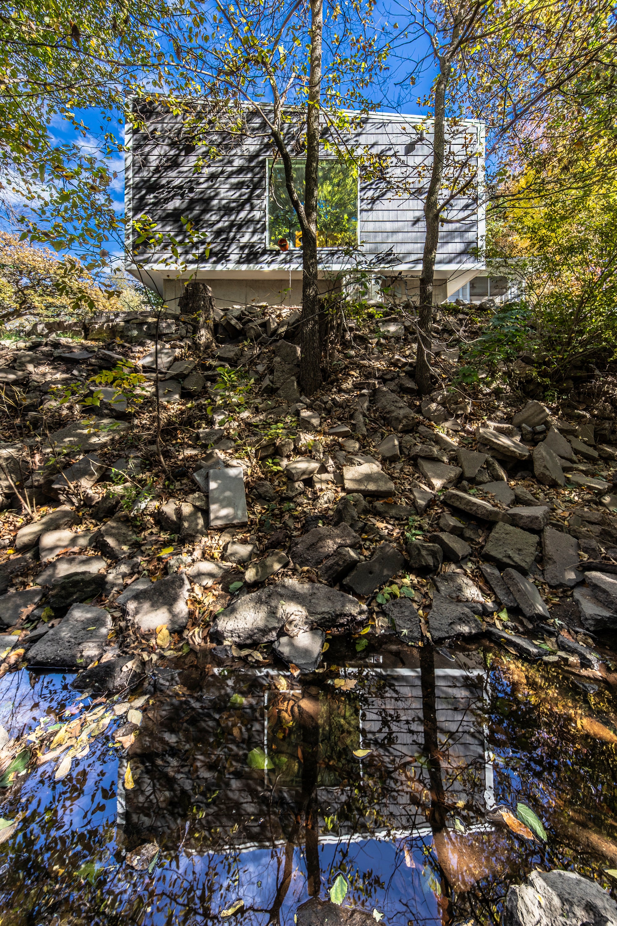 Modern house addition reflecting in adjacent creek with rocky terrain and trees around