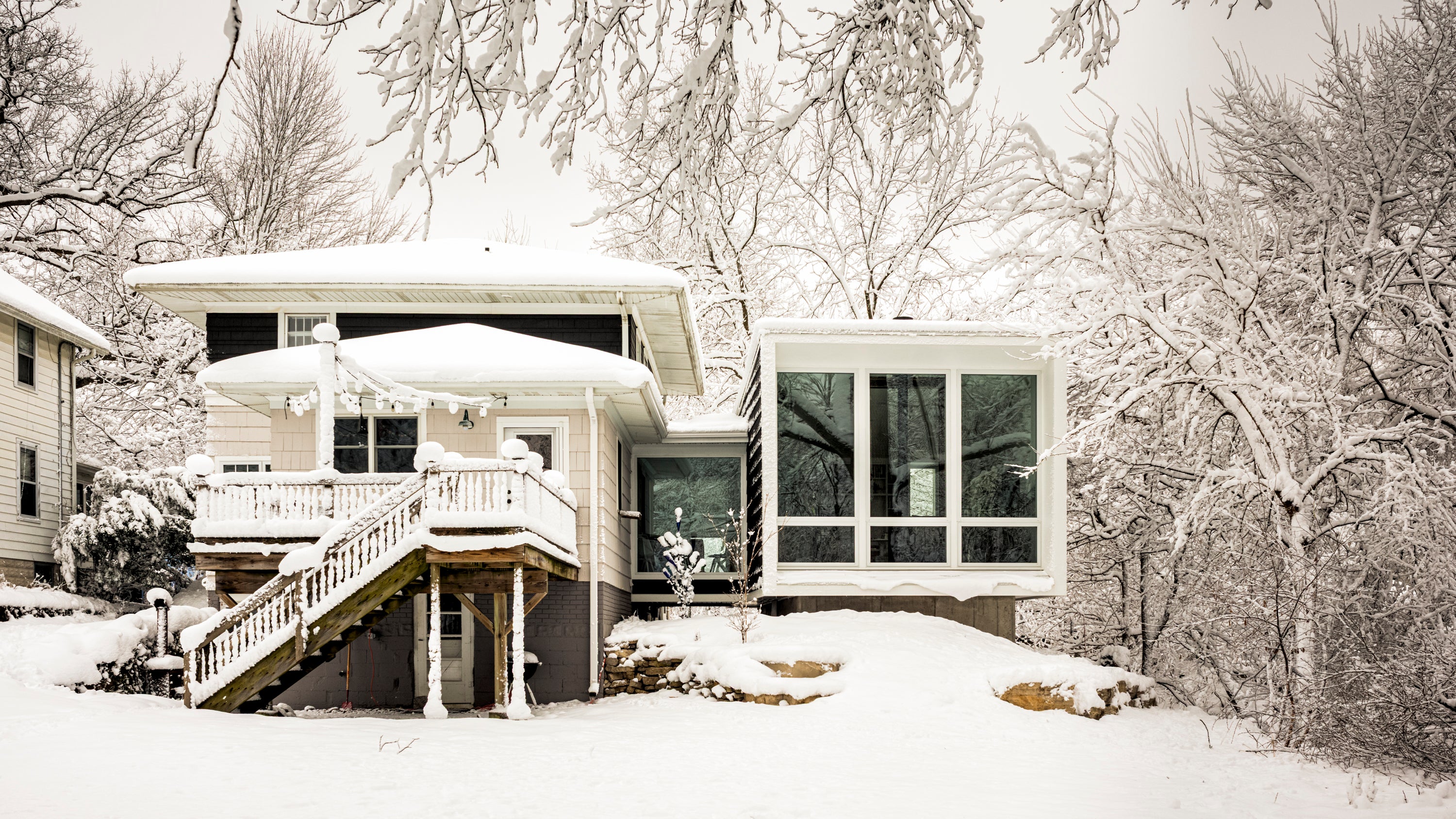 Modern house addition with a snow-covered roof and surrounding trees in winter.