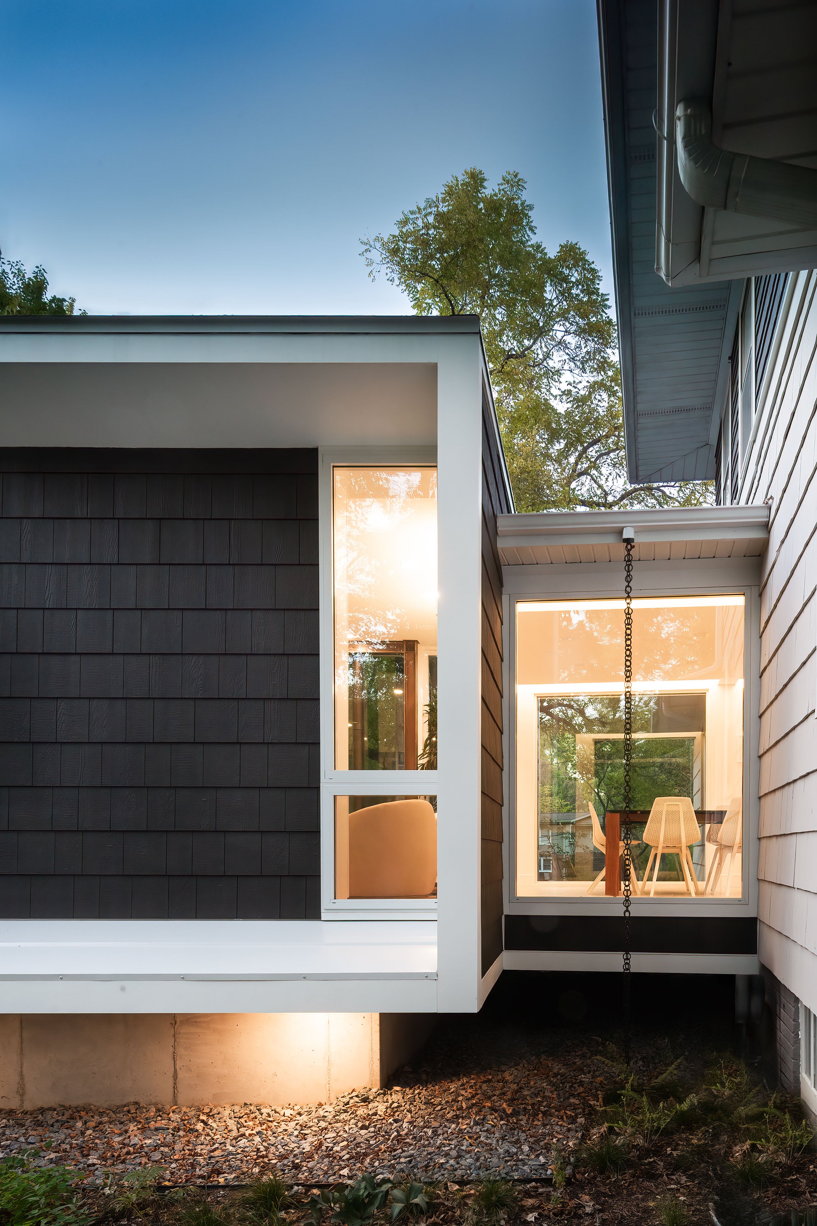 Modern house exterior with large windows and a well-lit interior.