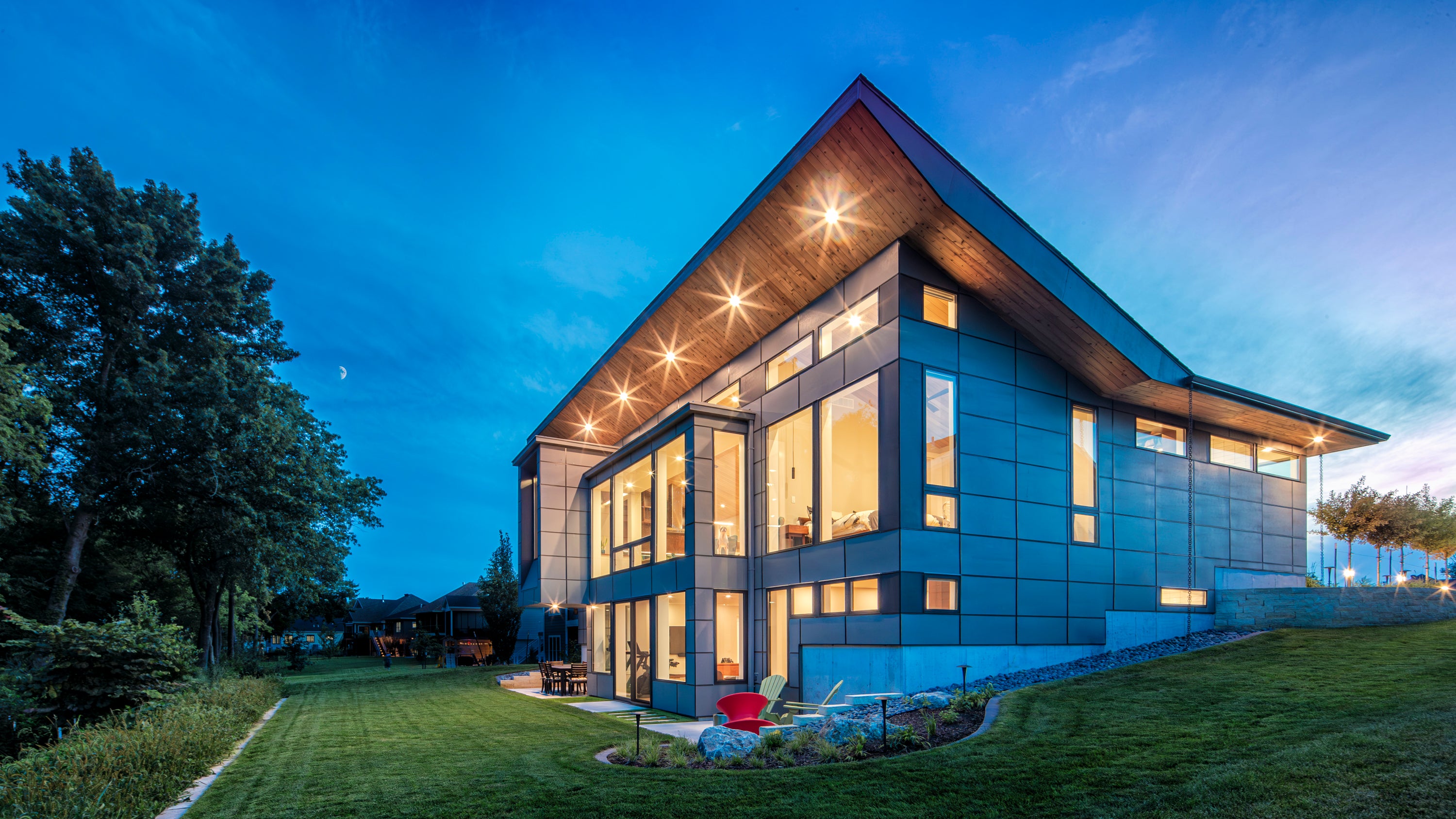 Modern house with large windows at dusk, surrounded by trees.