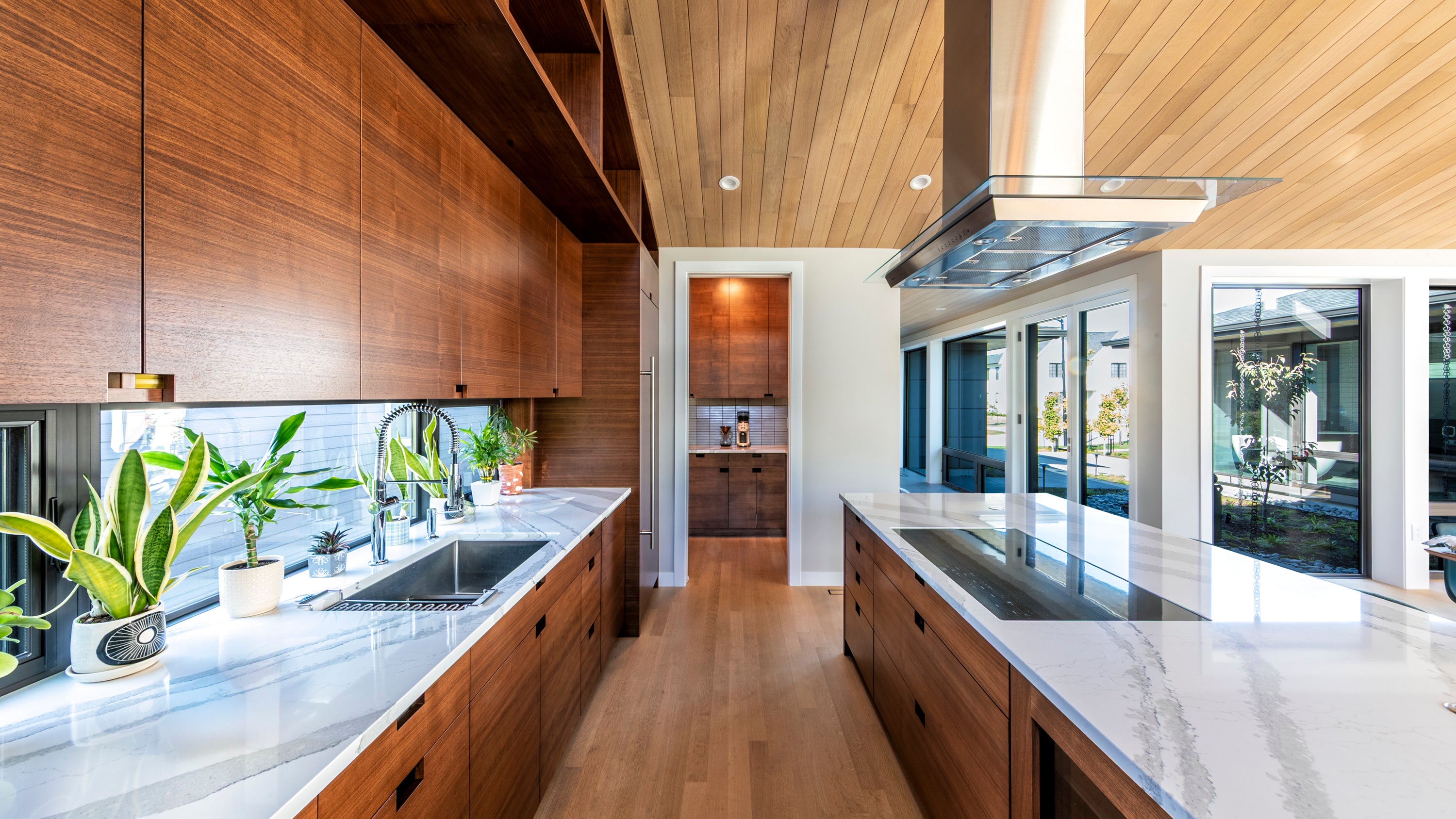 Modern kitchen with wooden cabinets, marble countertops, and large windows.