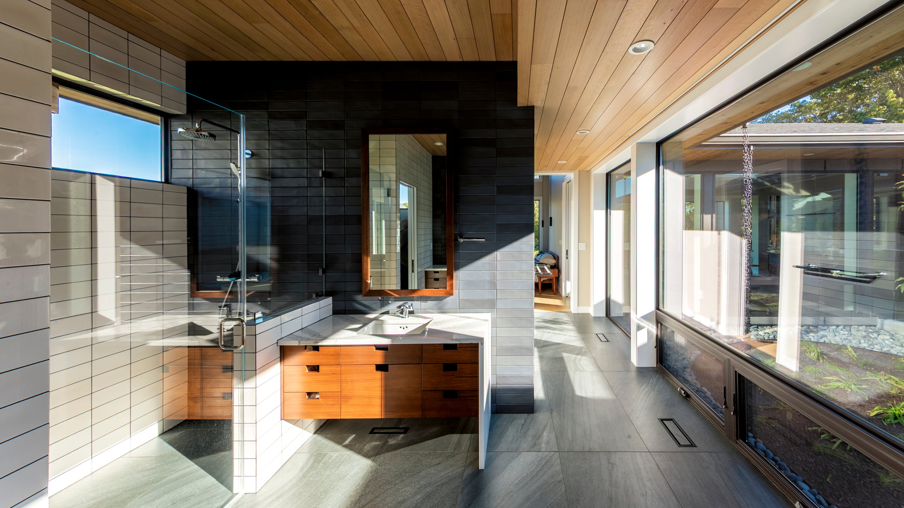 Modern bathroom with wooden vanity, large mirror, and large windows.