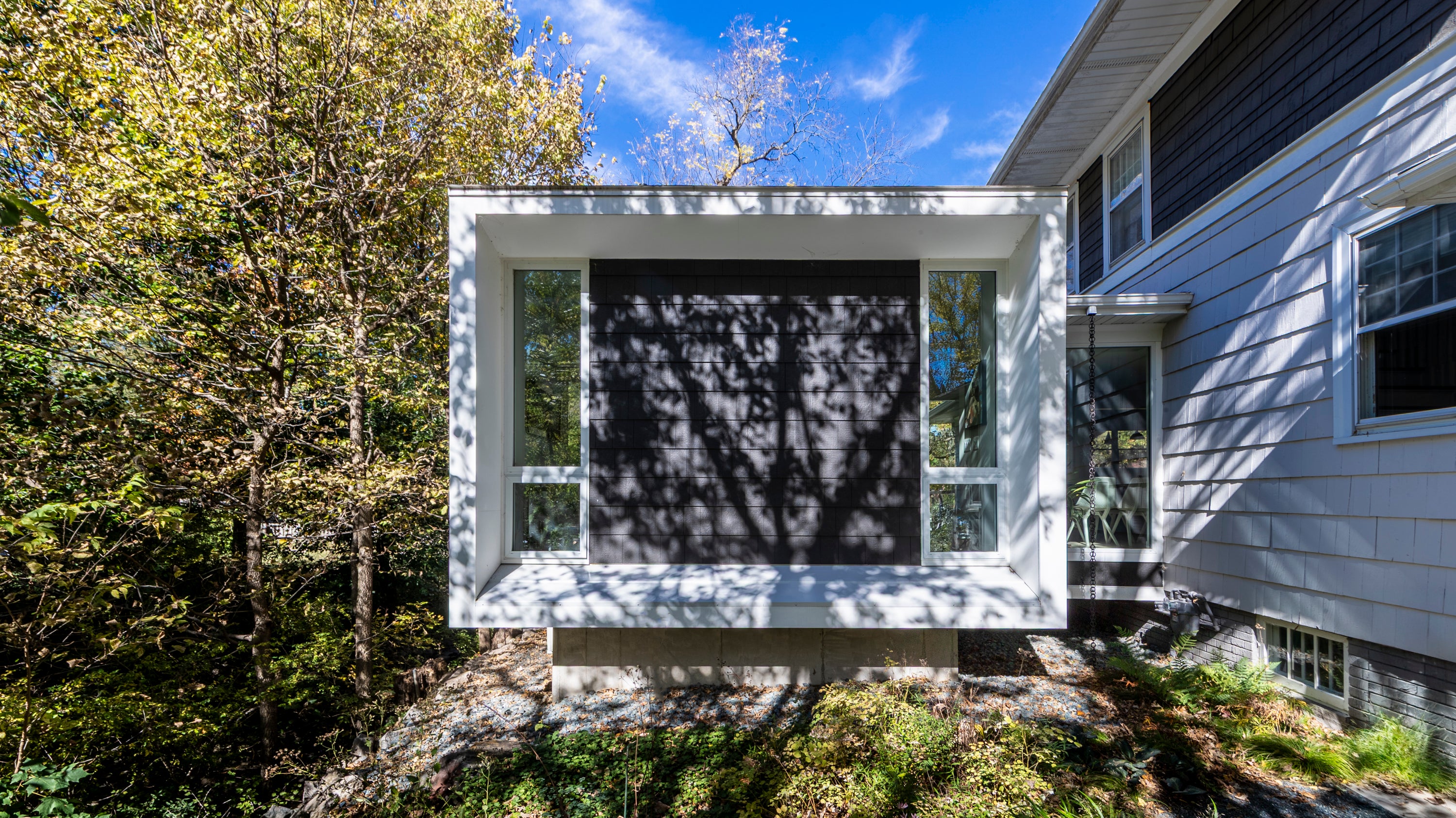 Modern house addition with a large window reflecting trees and sky