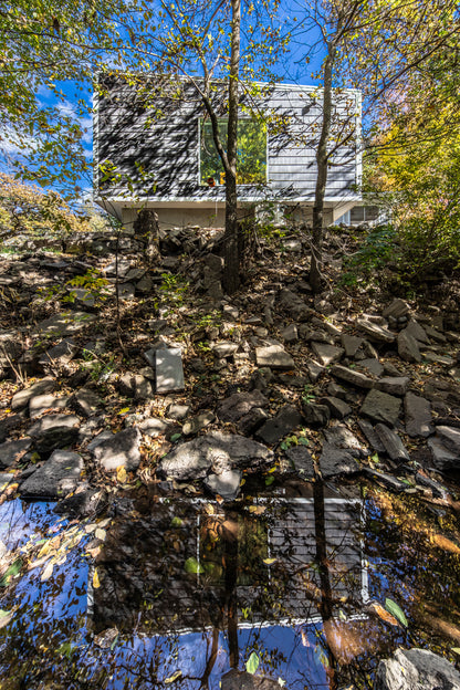 Modern house addition reflecting in adjacent creek with rocky terrain and trees around