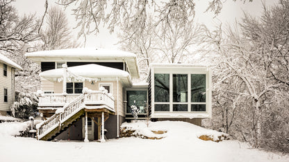 Modern house addition with a snow-covered roof and surrounding trees in winter.