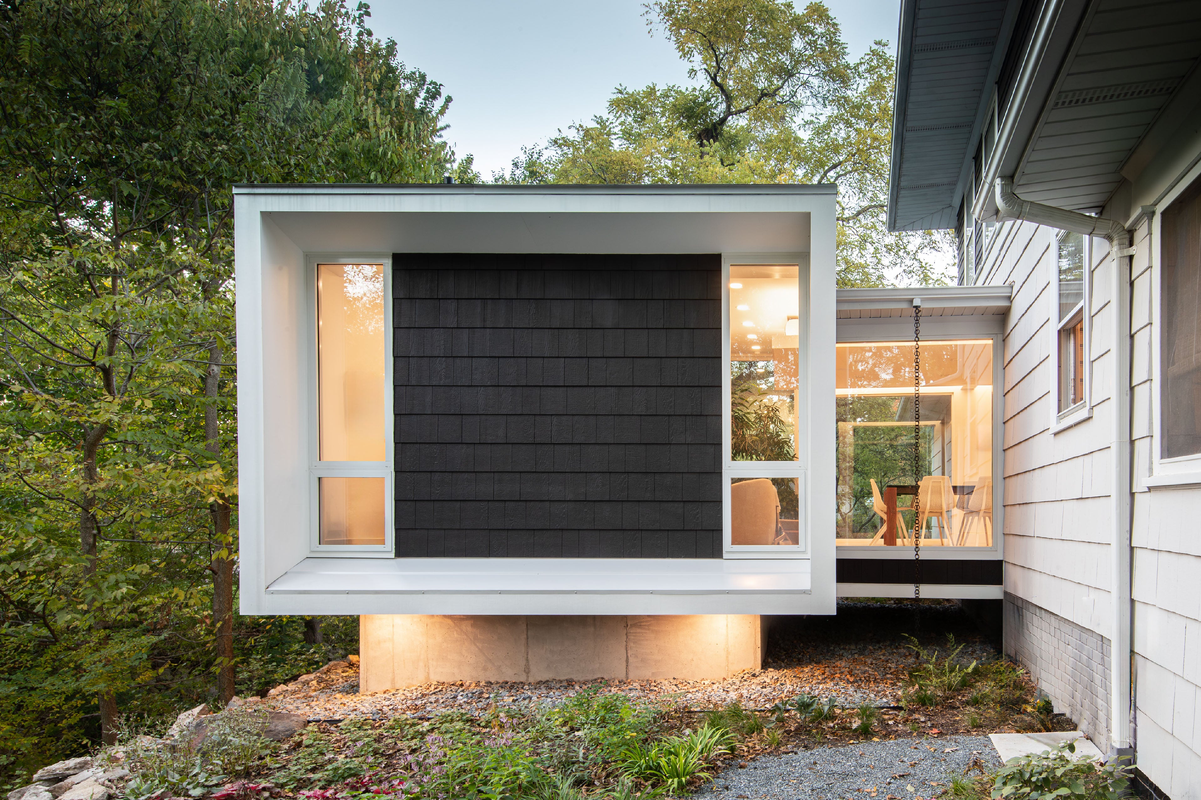 Modern house extension with glass walls and black cladding, surrounded by trees.