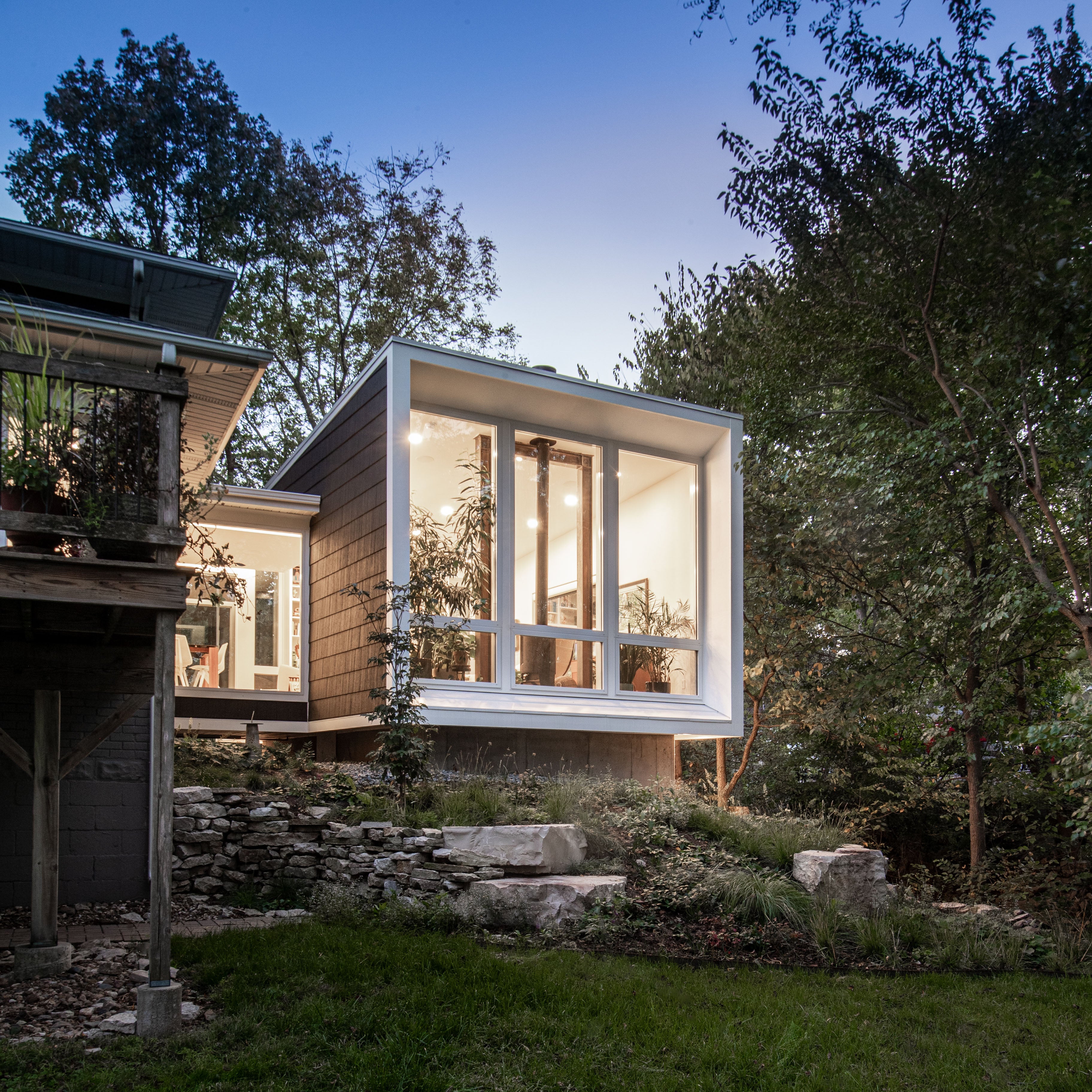 Modern house addition with large glass windows surrounded by trees