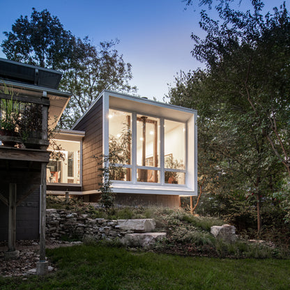 Modern house addition with large glass windows surrounded by trees