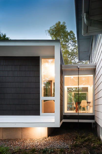 Modern house exterior with large windows and a well-lit interior.