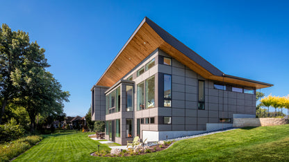 Modern Prairie style house with glass facade and wooden roof against a clear blue sky