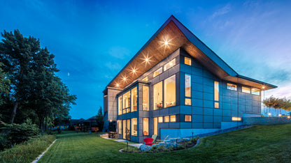 Modern house with large windows at dusk, surrounded by trees.