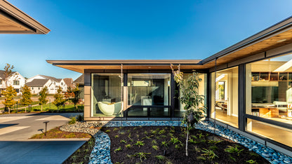 Modern house courtyard with large glass windows and a clear blue sky.