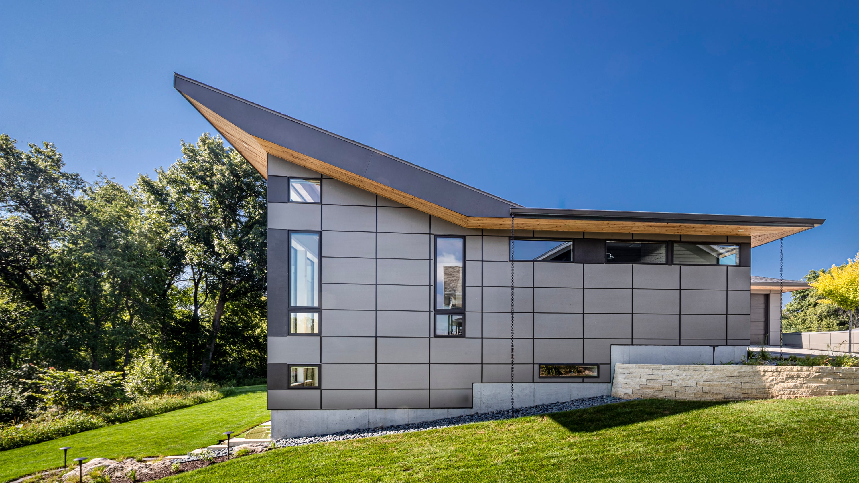 Modern Prairie style house with a sloped roof and glass windows, surrounded by greenery.