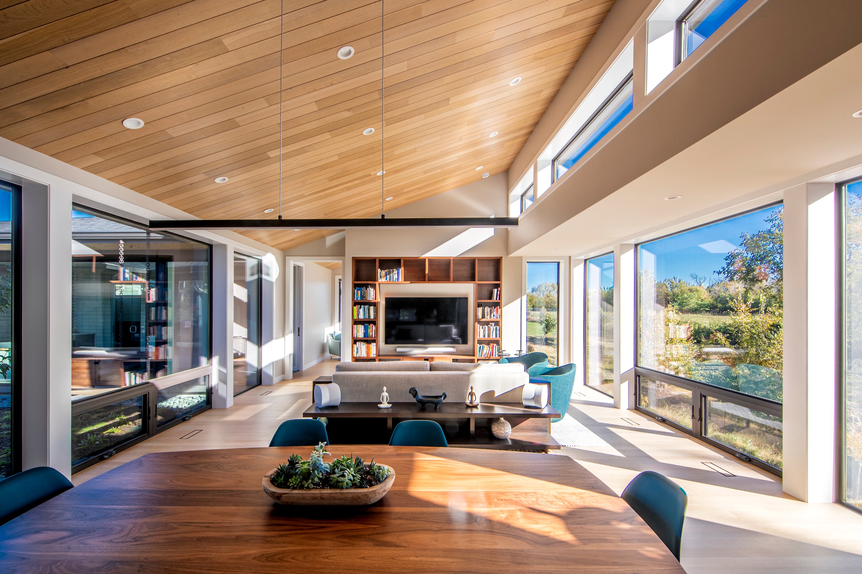 Modern living room with large windows, wooden dining table, and comfortable seating.