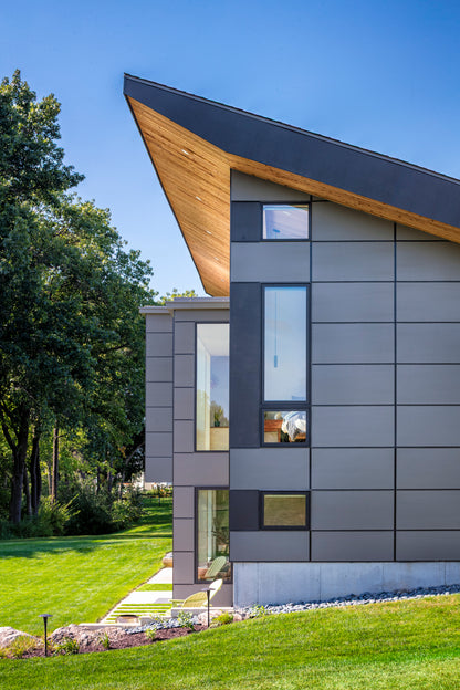 Modern house with gray facade and wooden roofline, surrounded by greenery.