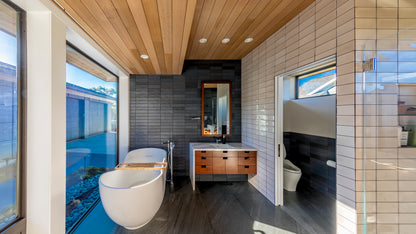 Modern bathroom with wooden ceiling, large windows, and white fixtures.